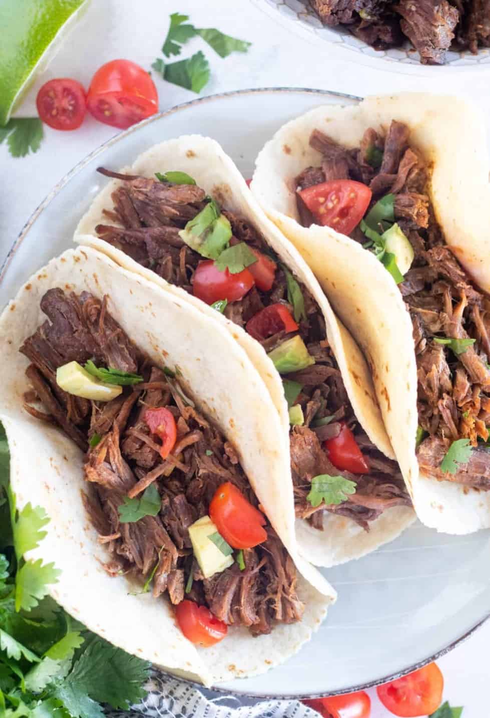 Three soft tacos filled with shredded beef on a plate.