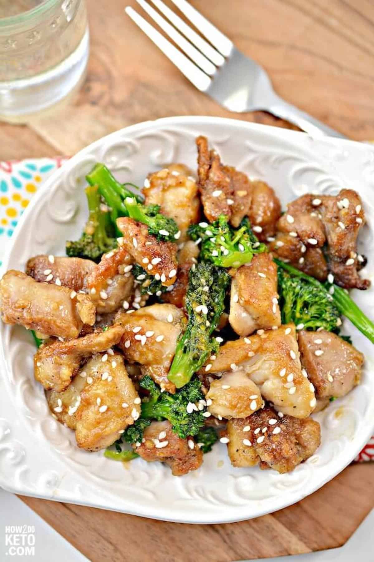 A white plate with chicken and broccoli topped with sesame seeds. 