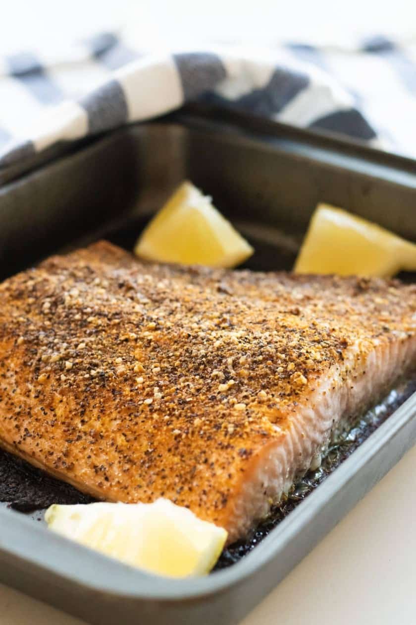 Salmon in a baking pan with lemon wedges. 