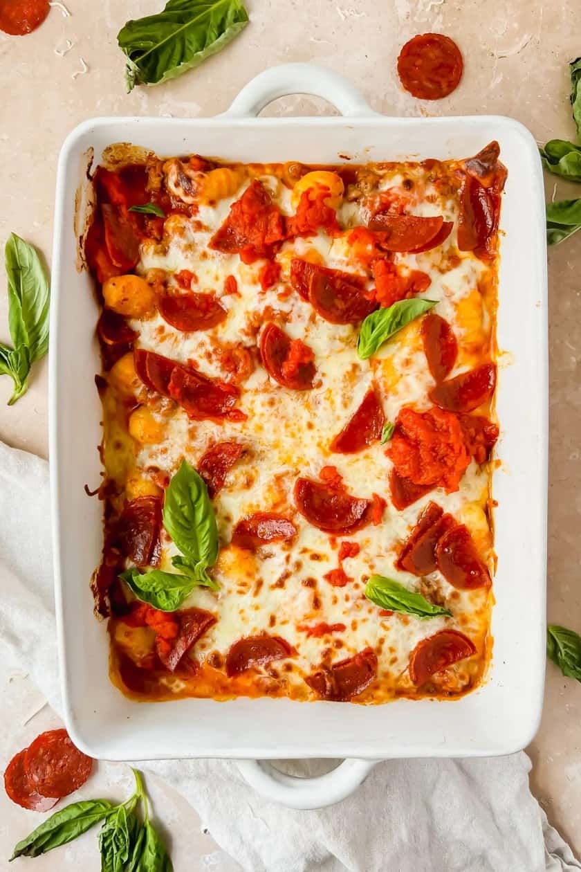 Pizza gnocchi prepared in a white baking dish with basil and pepperoni. 