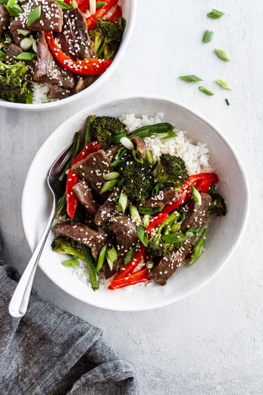 Two white bowls of beef stir fry with broccoli and peppers.
