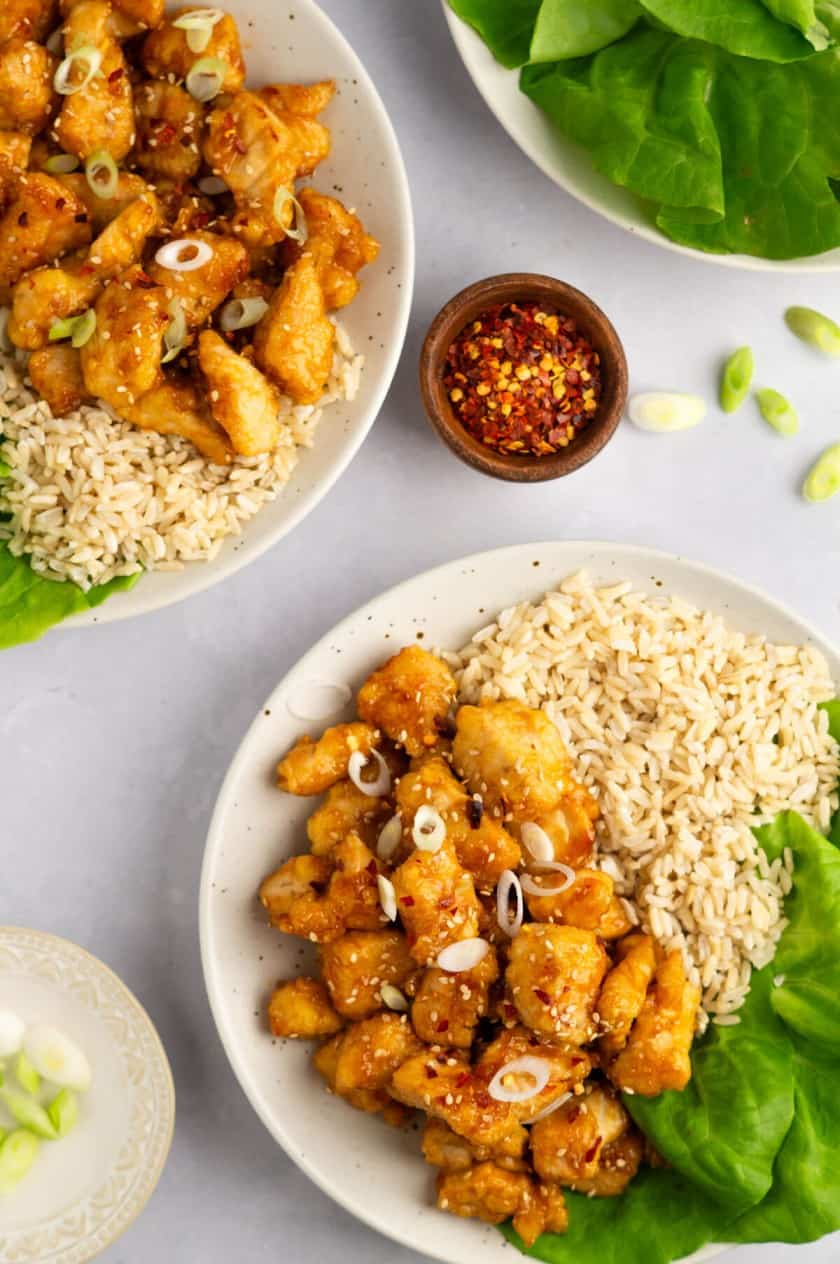 Two bowls of macro friendly orange chicken with rice and lettuce.