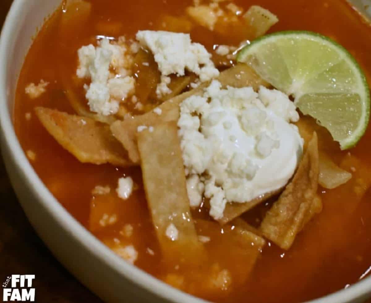 A macro-friendly bowl of tortilla soup with tortilla chips and a dollop of sour cream and a lime.