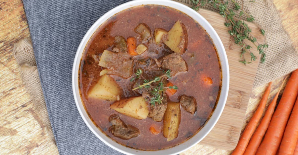 A bowl of beef stew with carrots and potatoes on a wooden table.