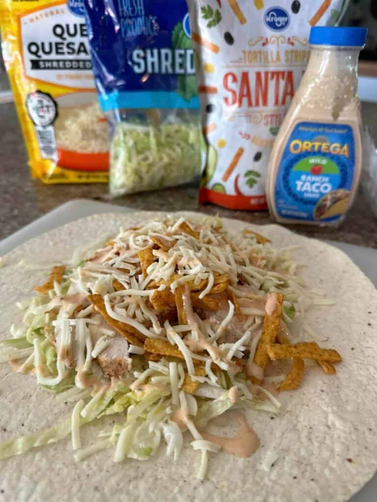 A healthy chicken wrap recipe featuring a tortilla filled with flavorful shredded chicken and topped with cheese and a dollop of creamy taco sauce on a cutting board.