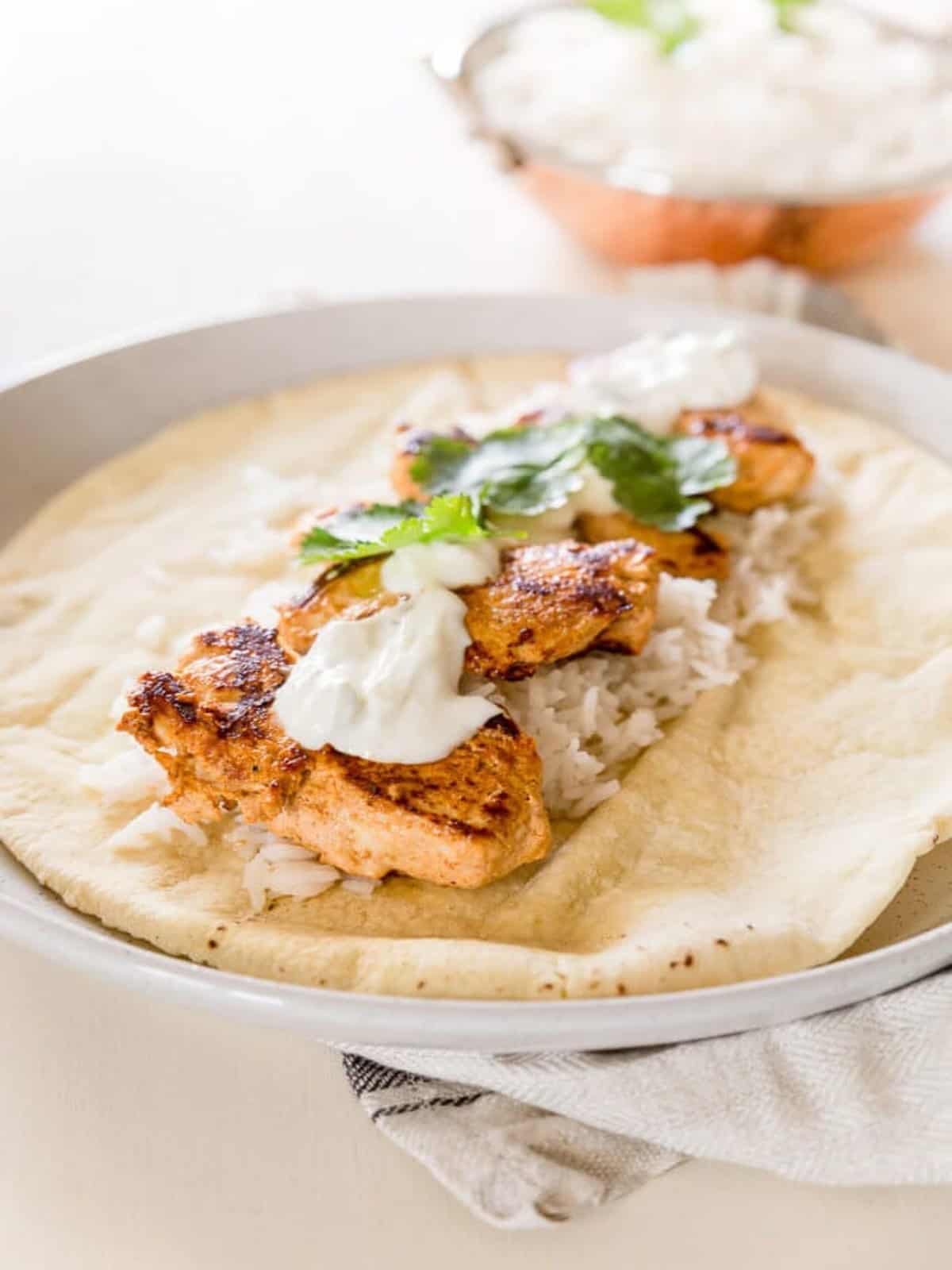 A tandoori chicken wrap with rice and a dollop of sour cream on a flatbread. 