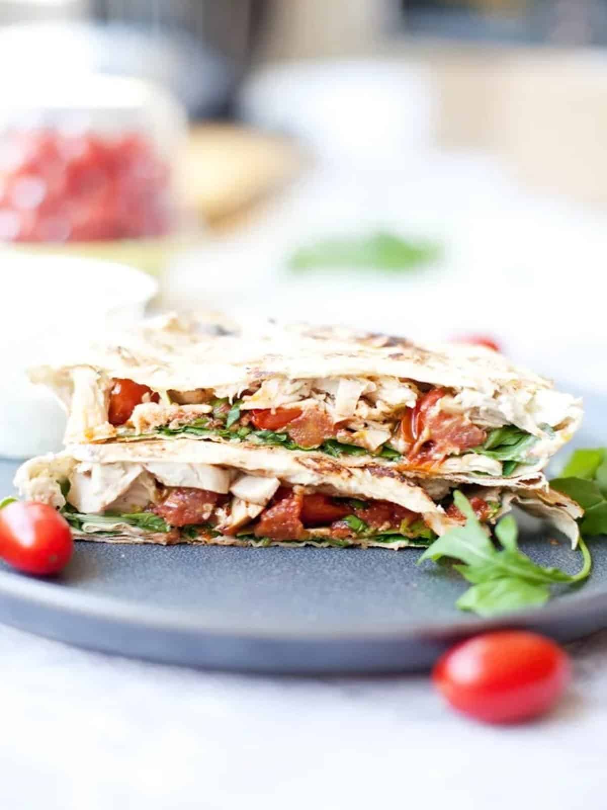 A tomato basil chicken crunch wrap with tomatoes and basil on a plate. 