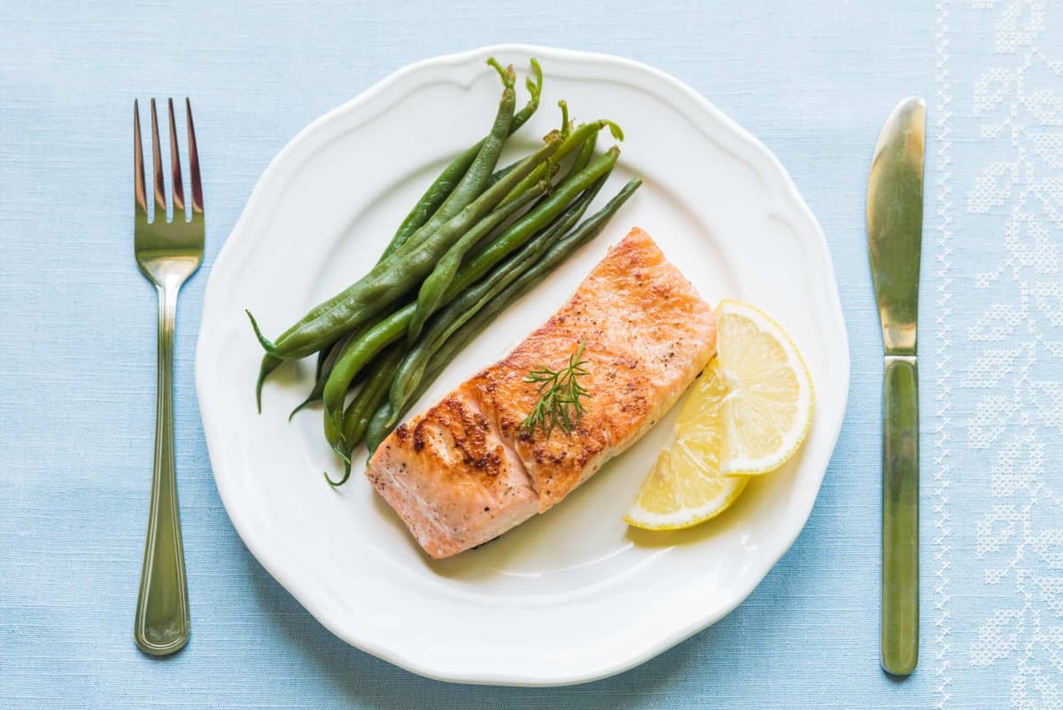 Grilled salmon on a plate with green beans and lemon. 