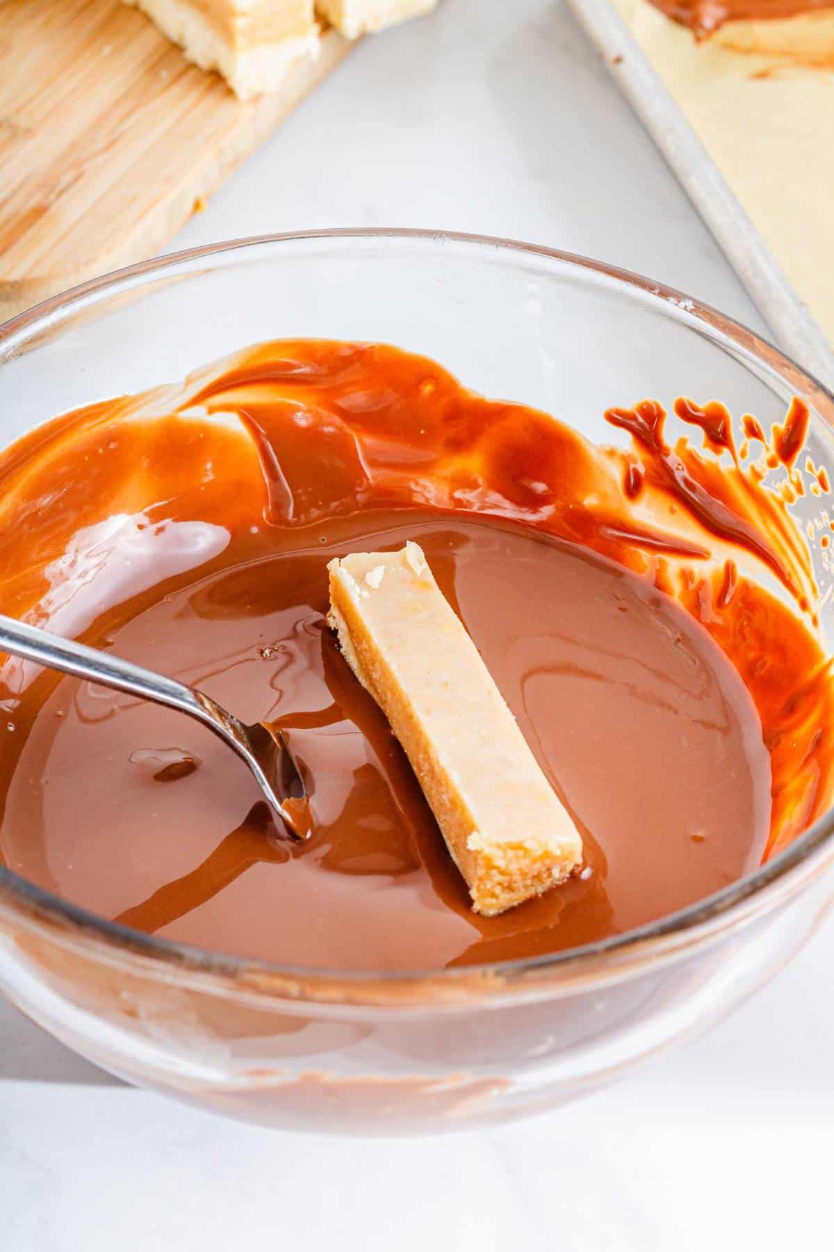 A glass bowl with Twix bars being dipped into melted chocolate. 