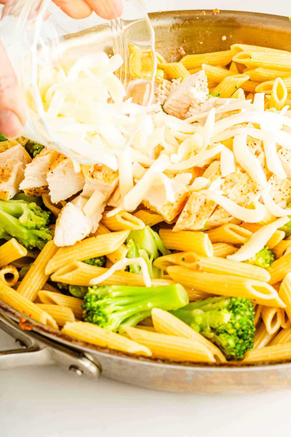 Mozzarella being put on top of penne pasta dish with chicken and broccoli.