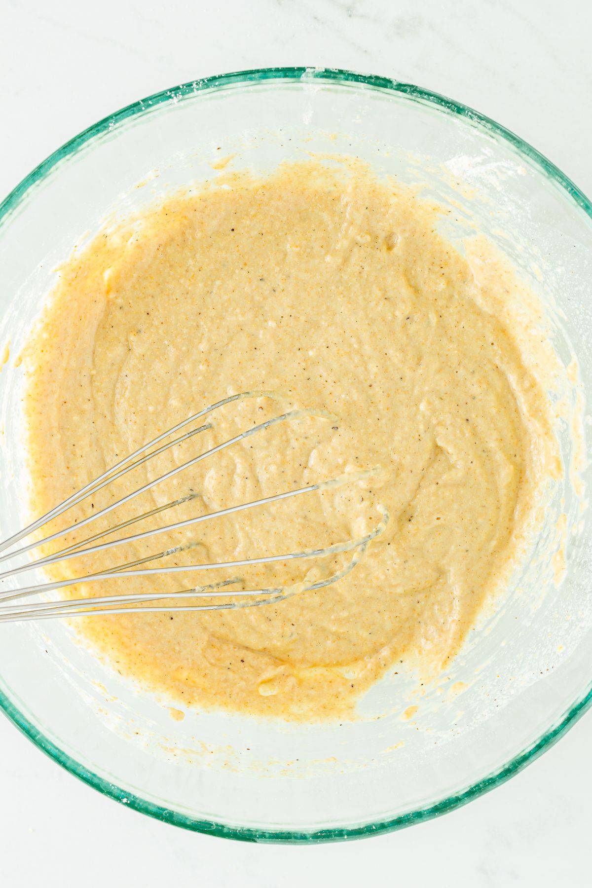 A bowl of pancake batter with a whisk in it. 