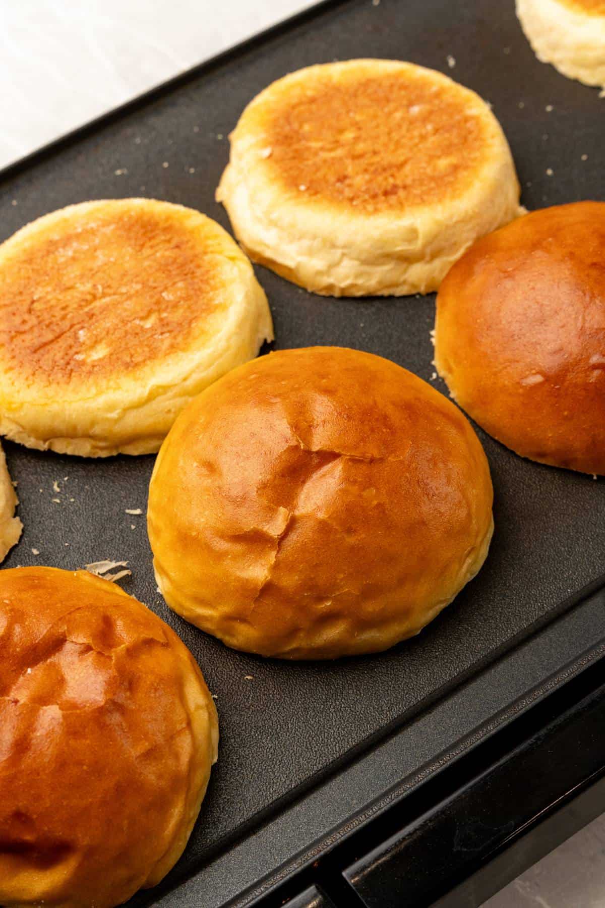 A griddle with with buns being toasted on it.