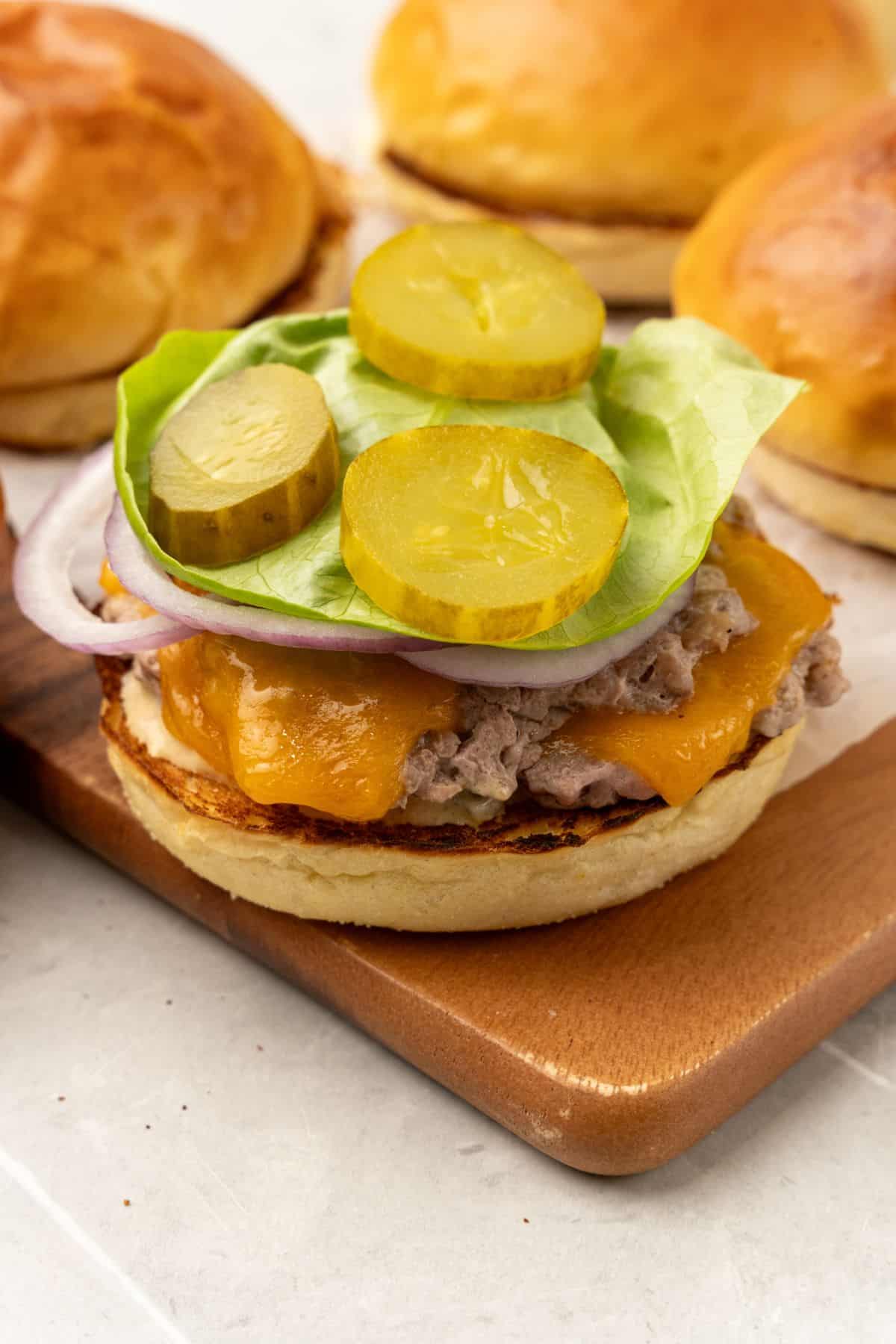 A wooden cutting board with turkey smash burgers and pickles on it.