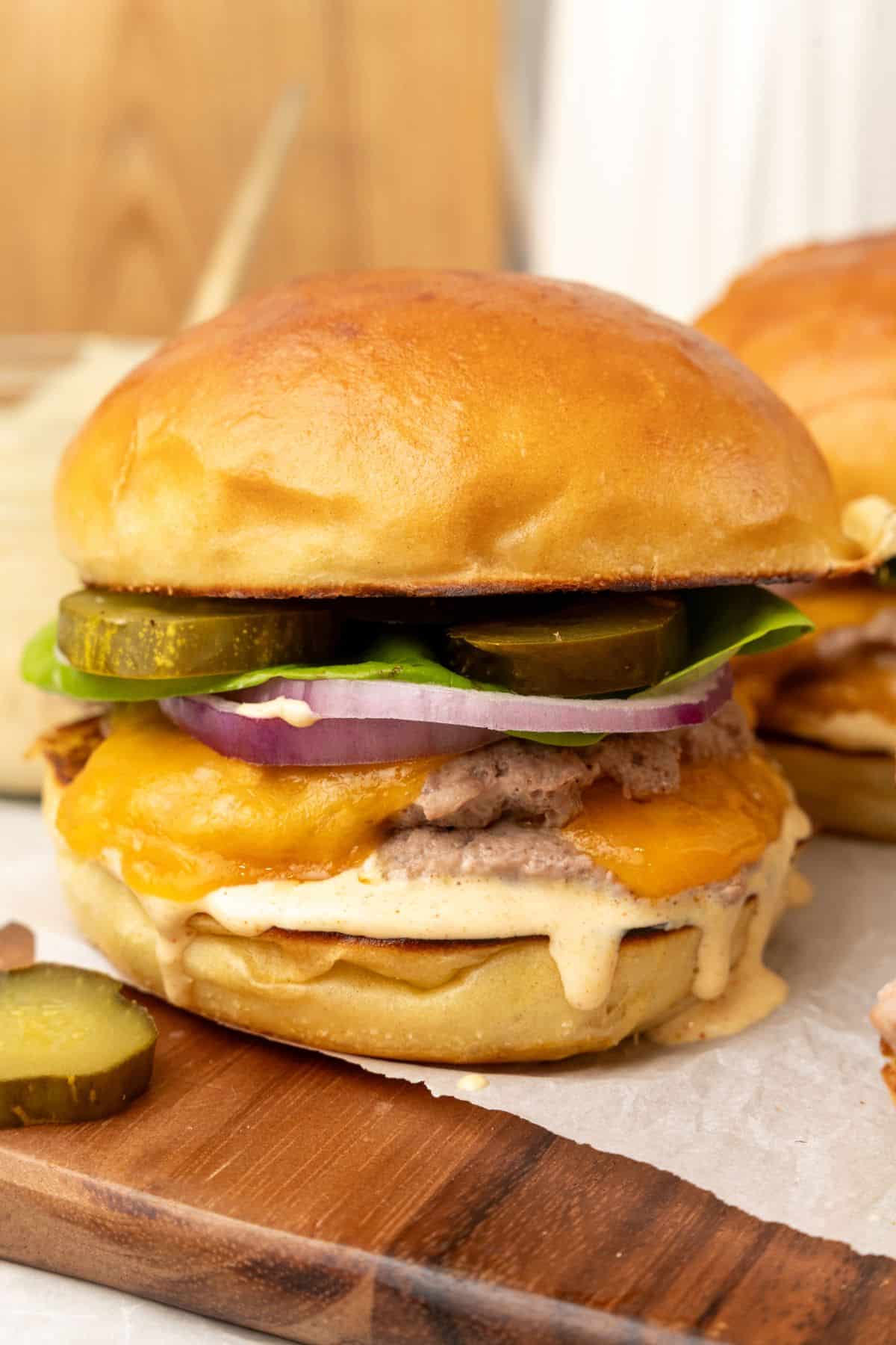 Two Turkey Smash Burgers with cheese and pickles on a cutting board.