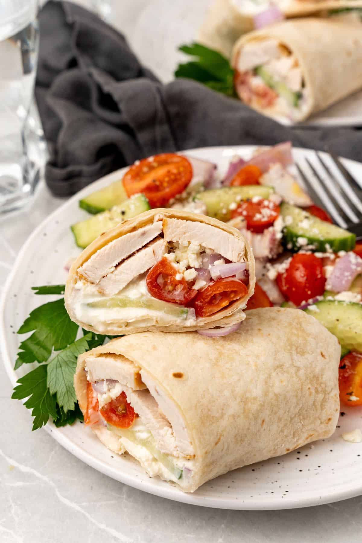 A Greek chicken wrap on white plate with cucumber. 