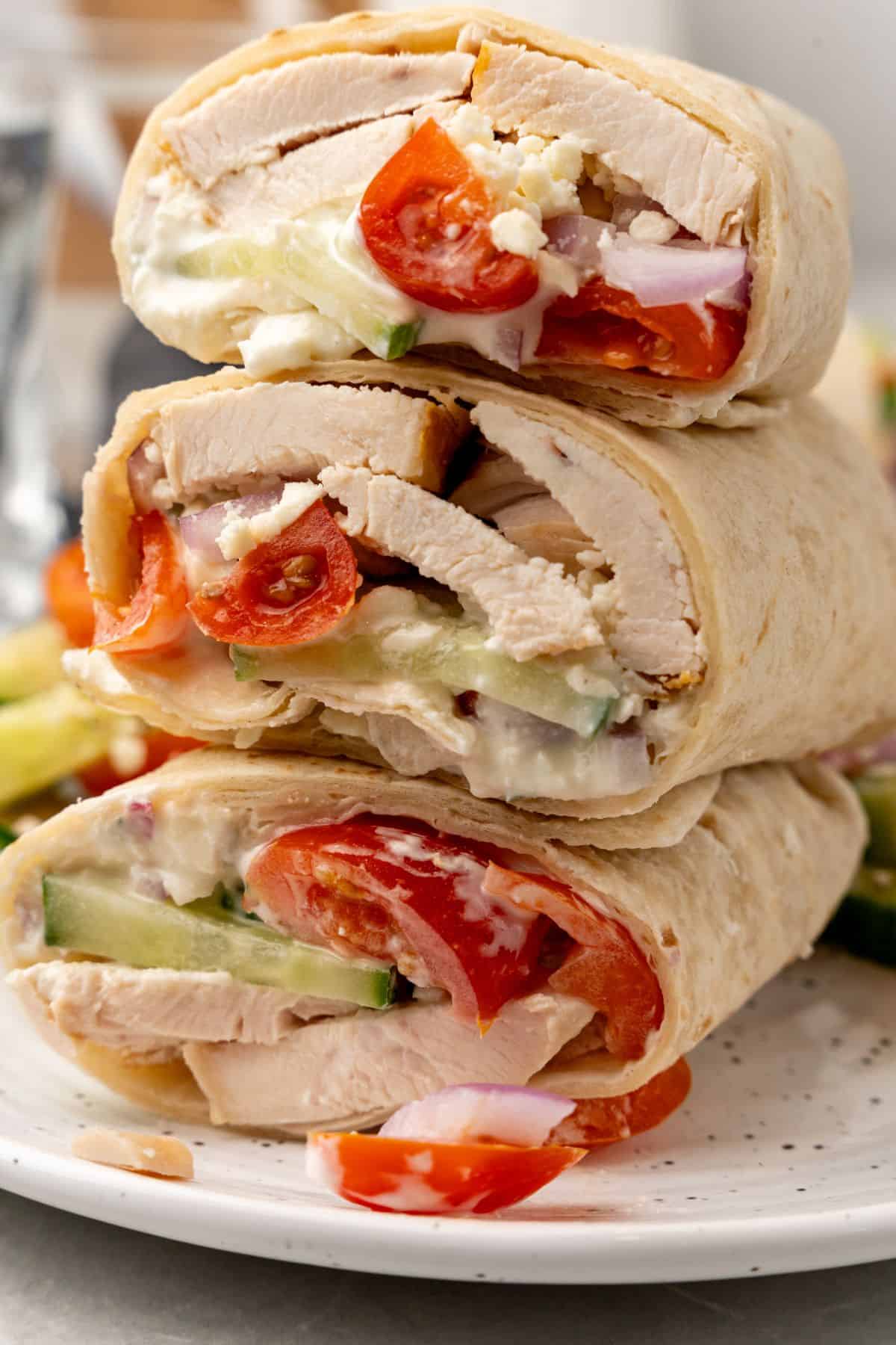 A stack of Greek chicken wraps on a white plate. 