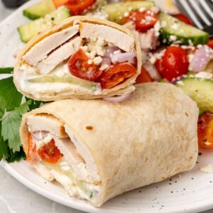 A Greek chicken wrap filled with strips of marinated chicken, accompanied by juicy tomatoes and refreshing cucumbers, elegantly presented on a plate.