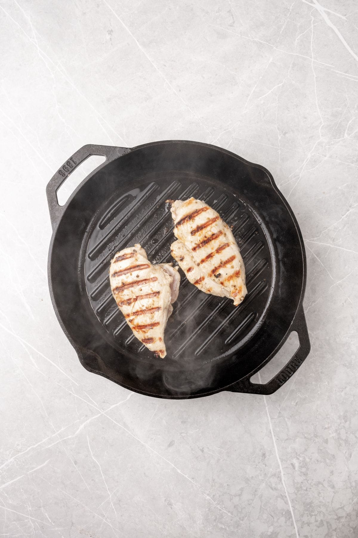 A pair of chicken breasts cooking on a grill pan. 