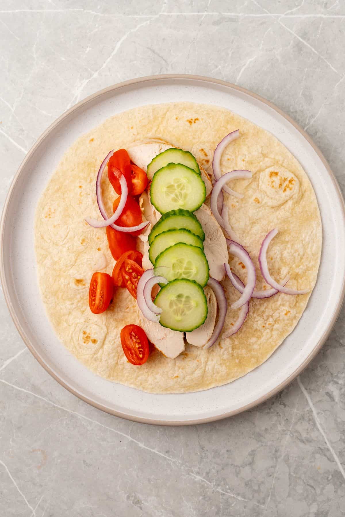 A Greek wrap with chicken, vegetables and meat on it.