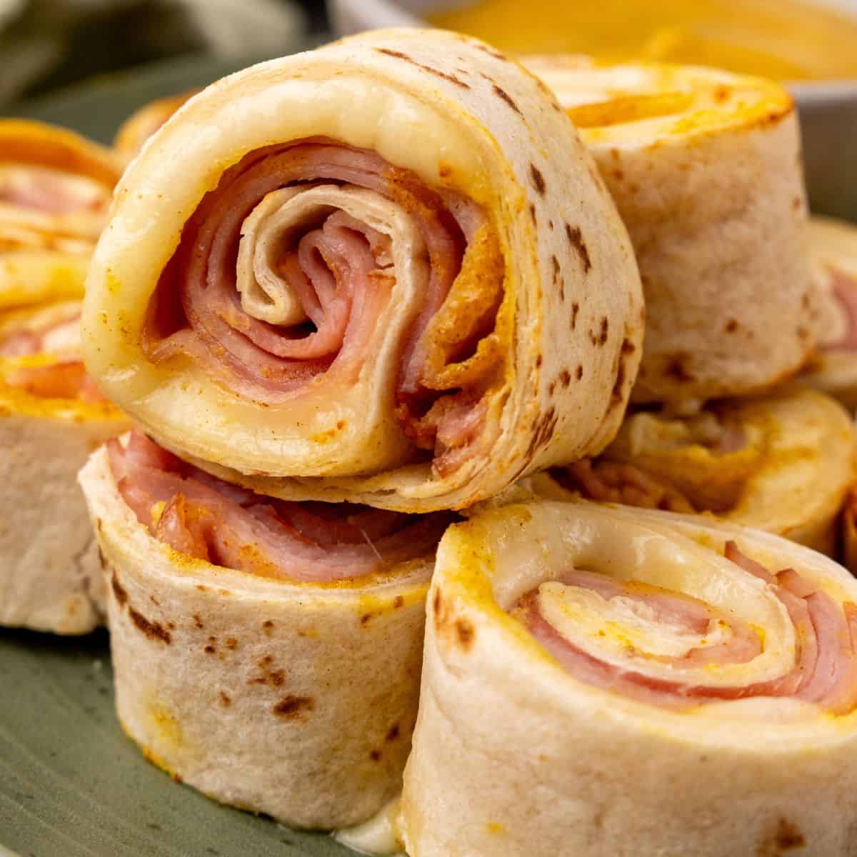 Ham and cheese wraps are neatly arranged on a plate.