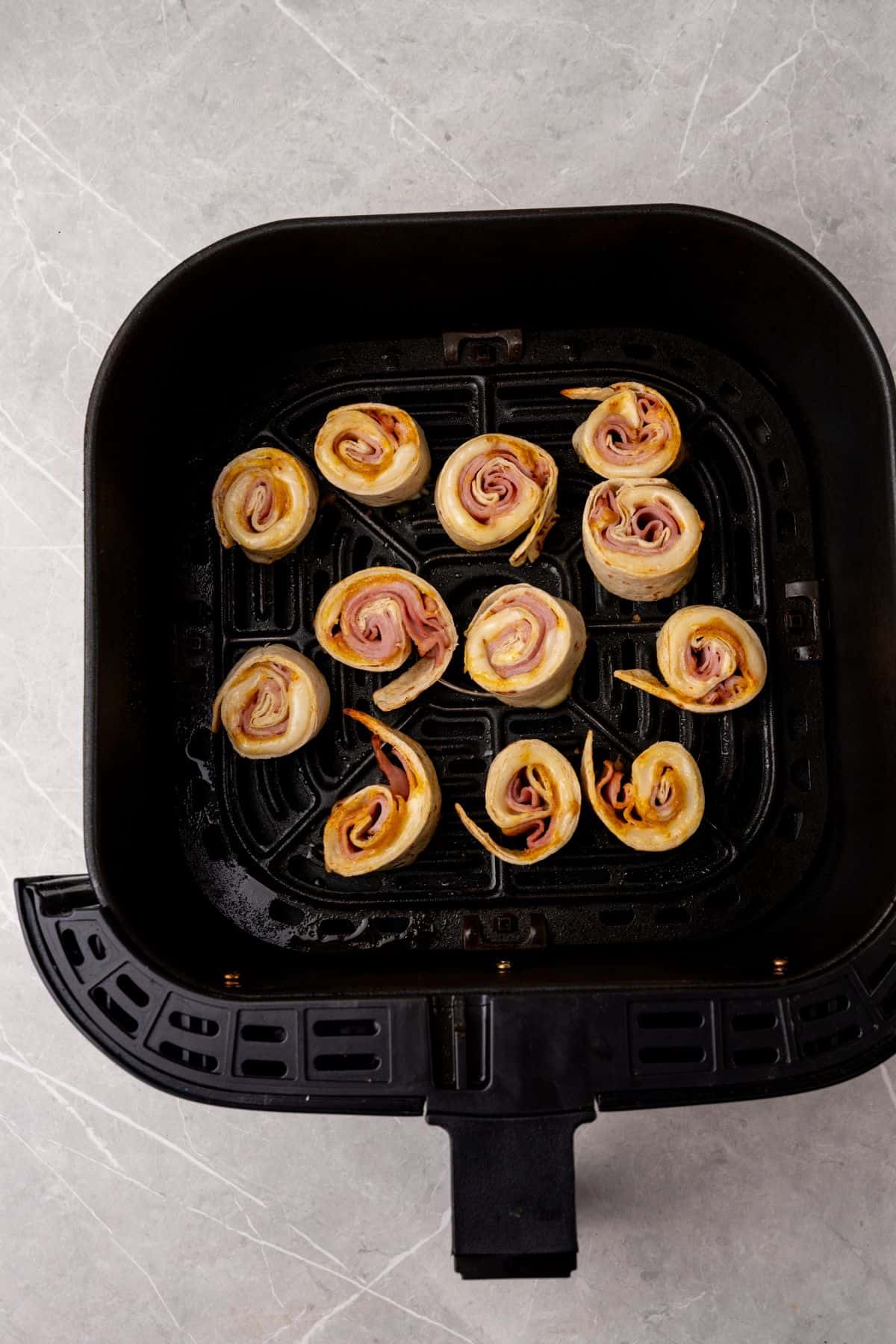 An air fryer filled with ham and cheese rolls.