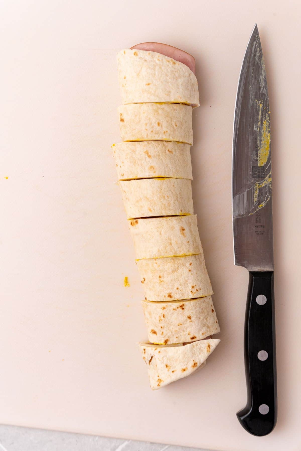 A knife next to a tortilla, ready to be filled with delicious wraps made of ham and cheese.