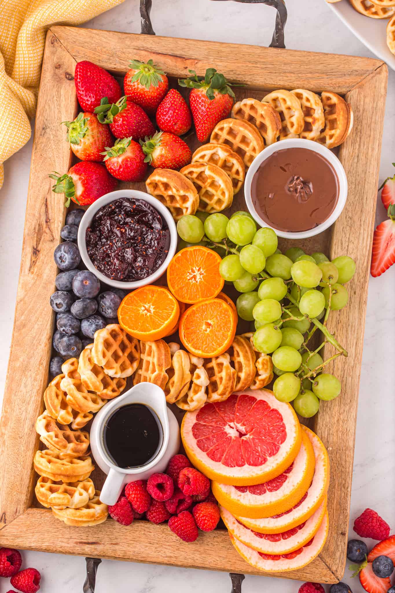A colorful array of breakfast foods including waffles, fresh fruit, and assorted spreads displayed on a wooden board.