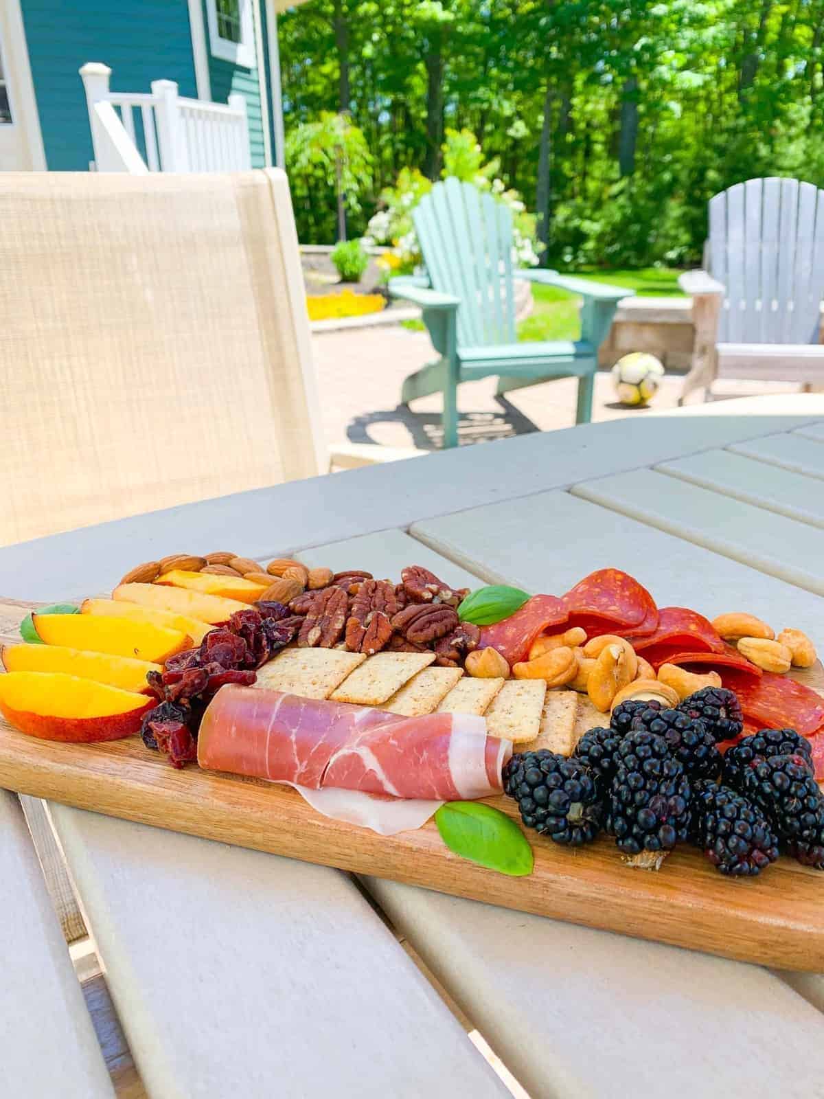 A charcuterie board with an assortment of meats, cheeses, fruits, and nuts on an outdoor patio table.