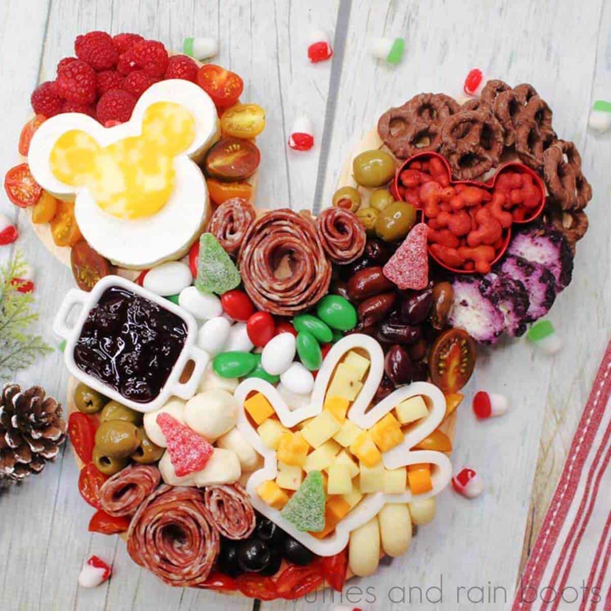 A colorful charcuterie board with a variety of sweets, fruits, and cured meats arranged in a whimsical, disney-inspired theme.