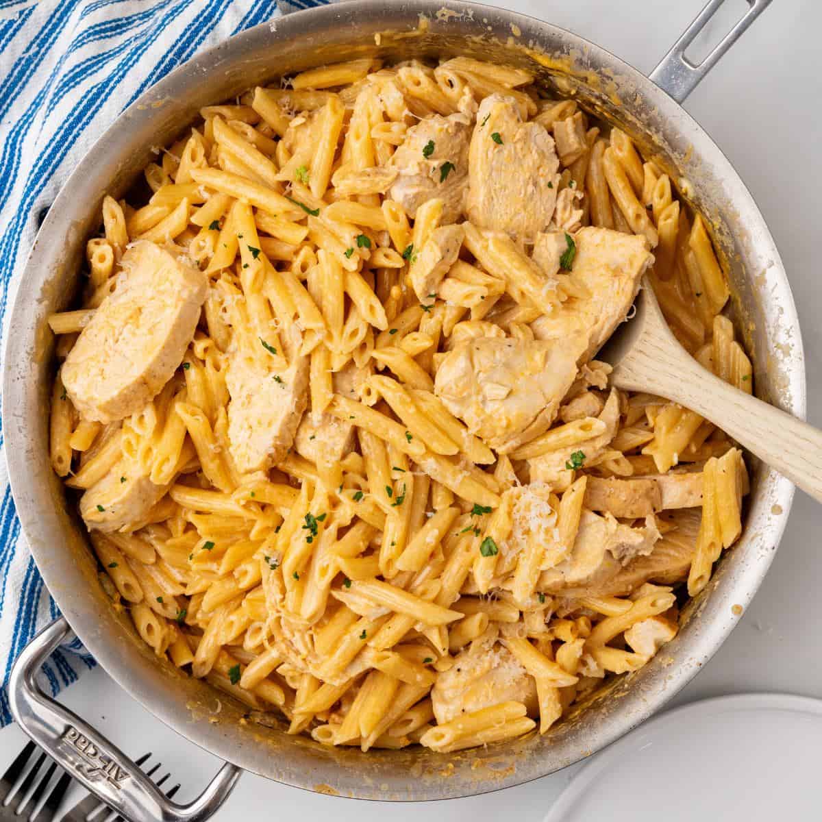 A skillet filled with creamy Buffalo Chicken Alfredo pasta, garnished with herbs, and a wooden spoon.