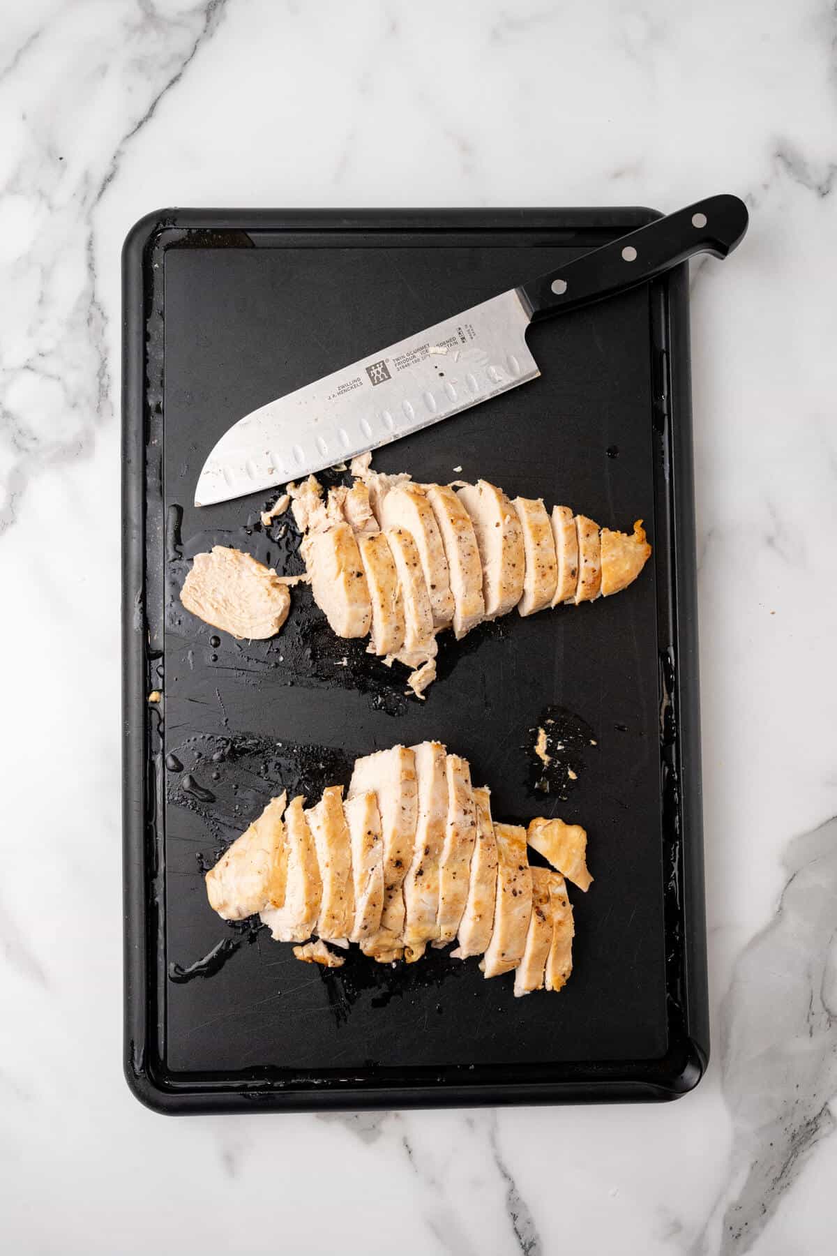 Sliced grilled chicken breast on a cutting board with a chef's knife.