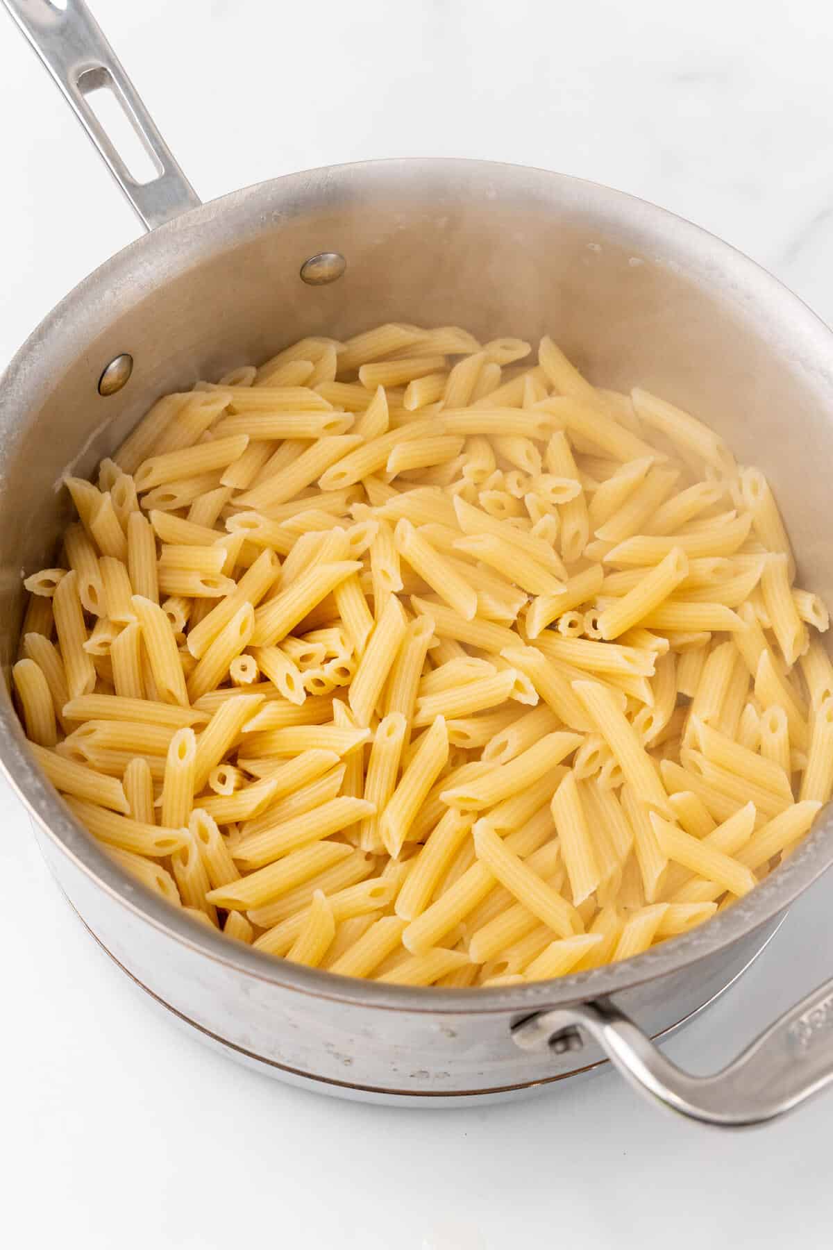 Penne pasta in a stainless steel pot.