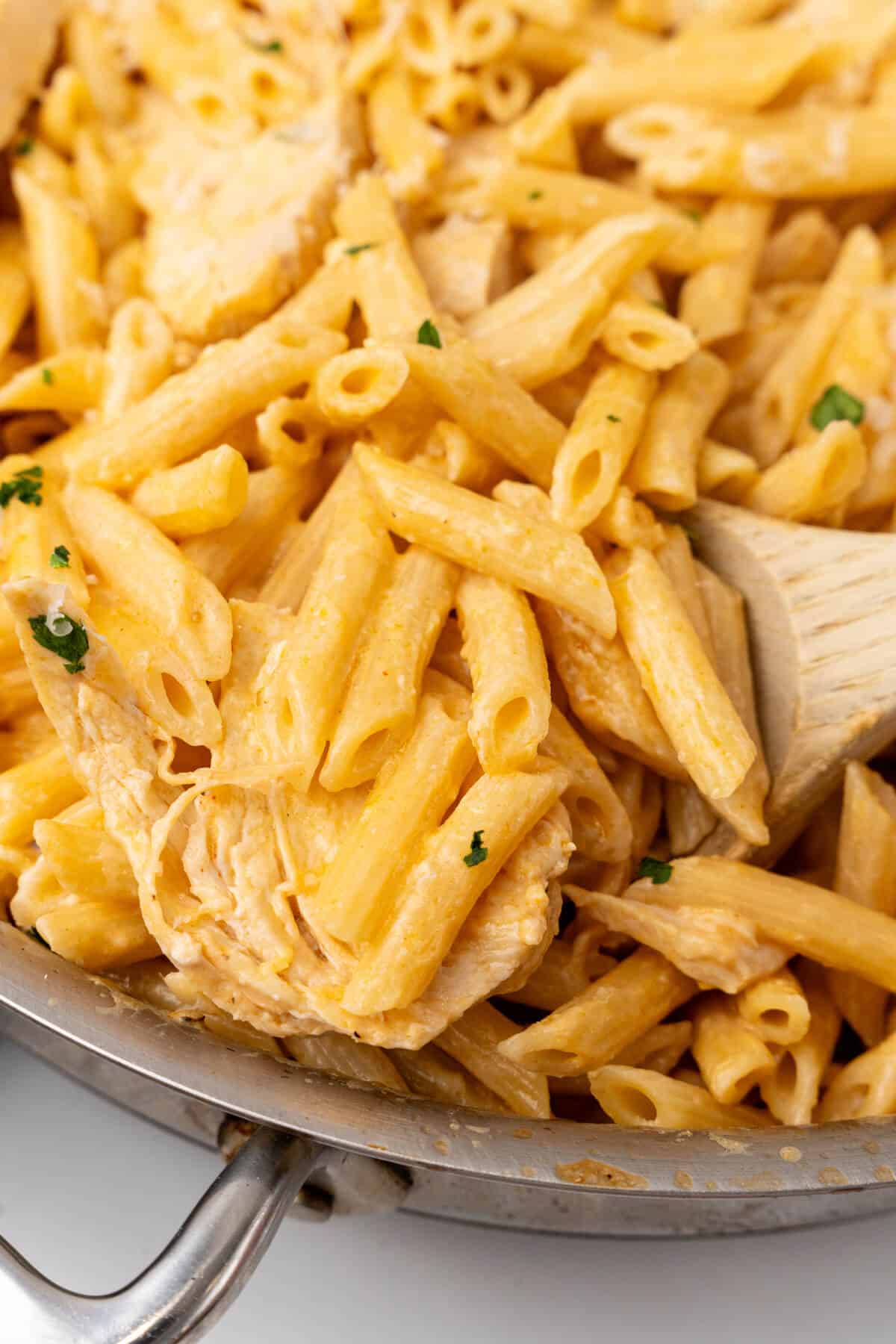 Creamy Buffalo Chicken Alfredo pasta dish in a skillet with a wooden spoon.