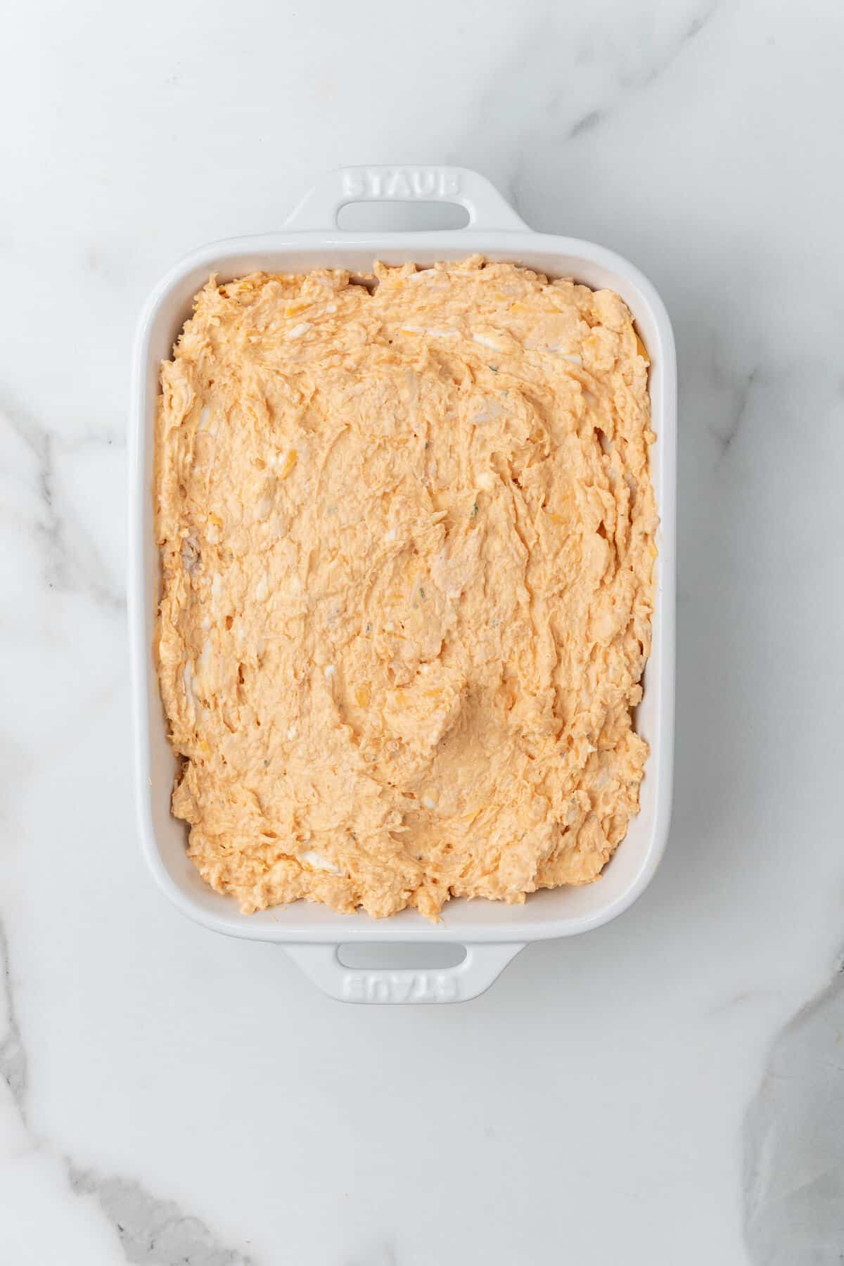 A cheesy dip with Buffalo Chicken in a white baking dish.