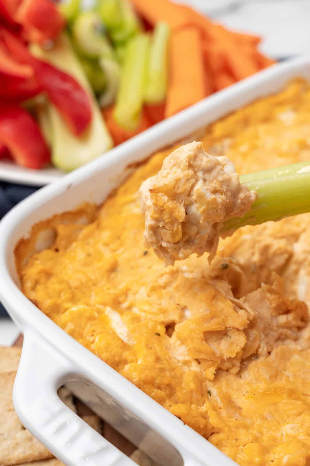 A Buffalo Chicken Dip being dipped into a dish with celery.