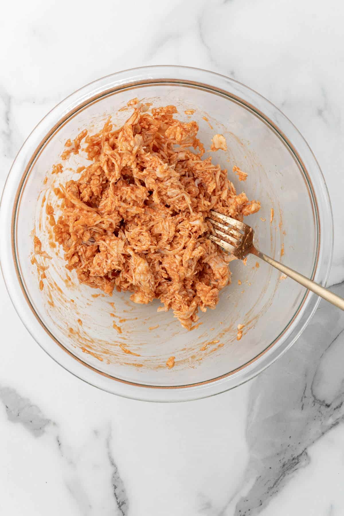 A bowl of shredded chicken with hot sauce. 