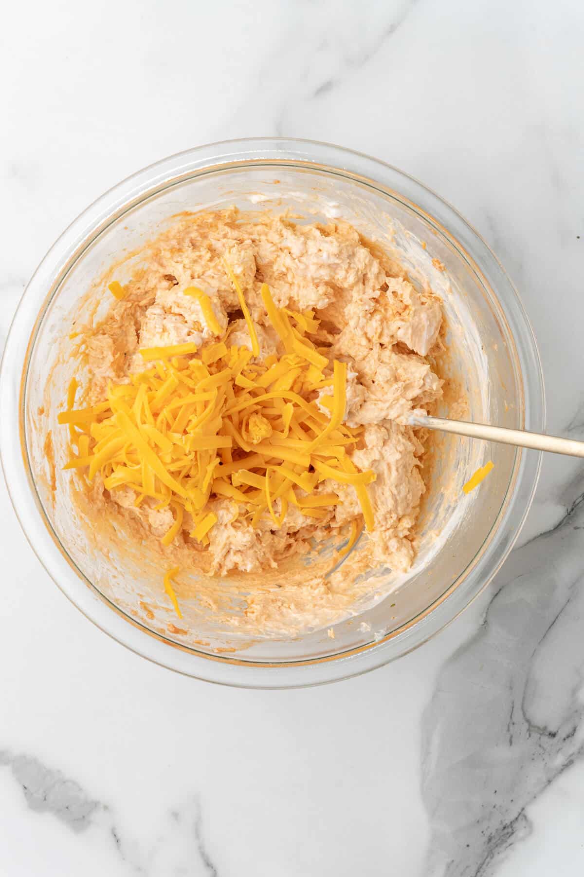 A bowl of buffalo chicken dip with shredded cheddar cheese. 