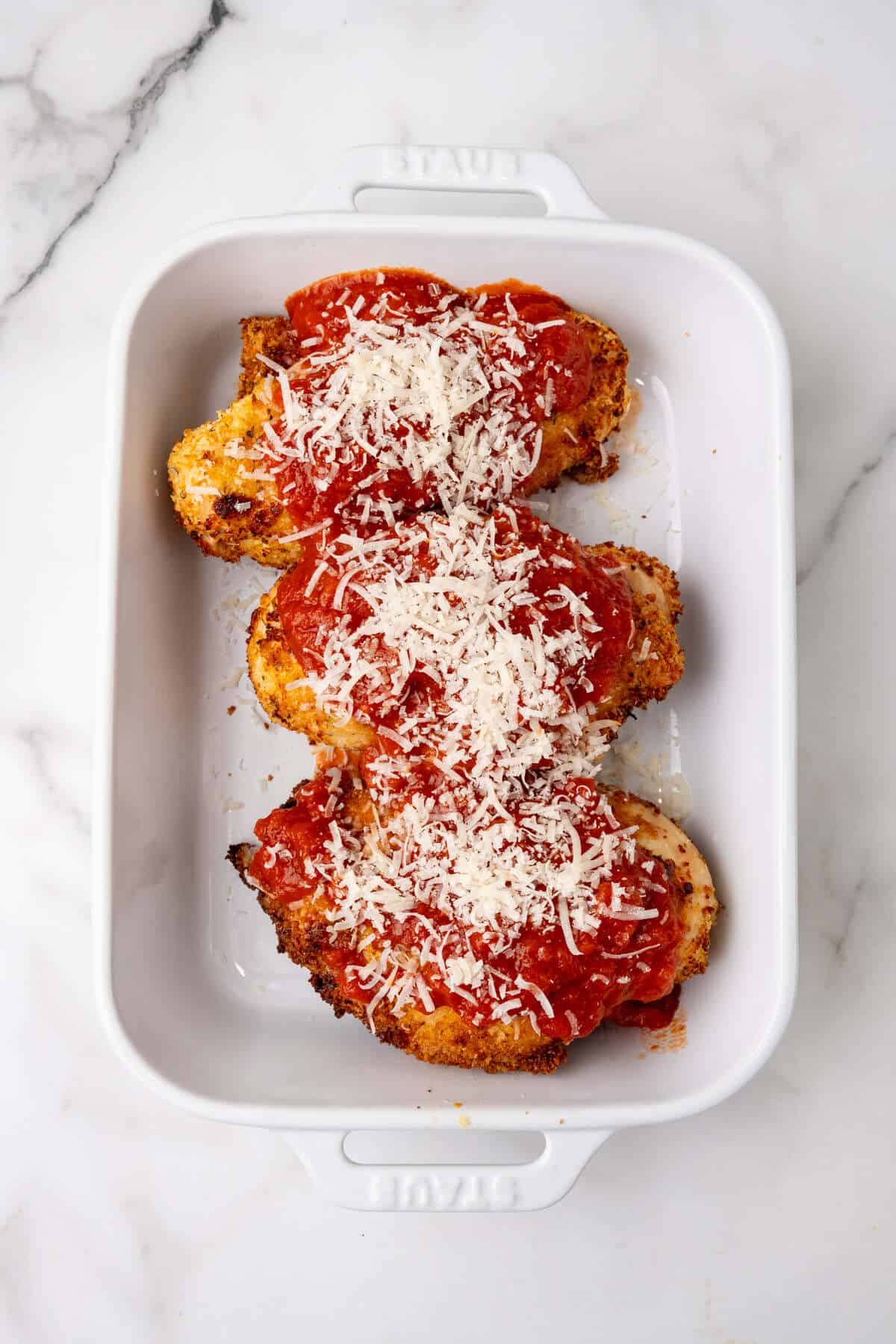 Chicken Parmesan Alfredo with melted cheese and tomato sauce in a white baking dish.