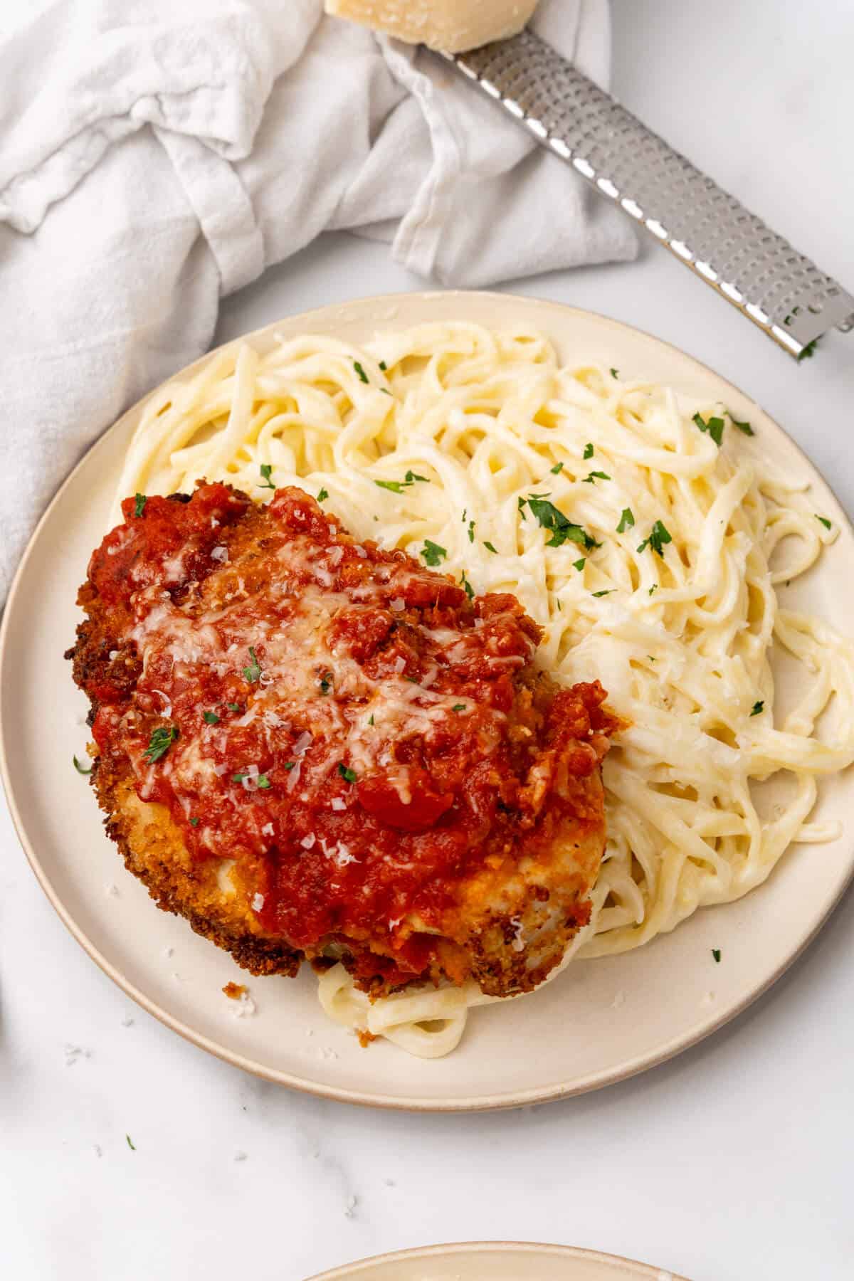 A plate of spaghetti topped with a breaded chicken cutlet and Alfredo sauce, garnished with grated cheese and parsley.