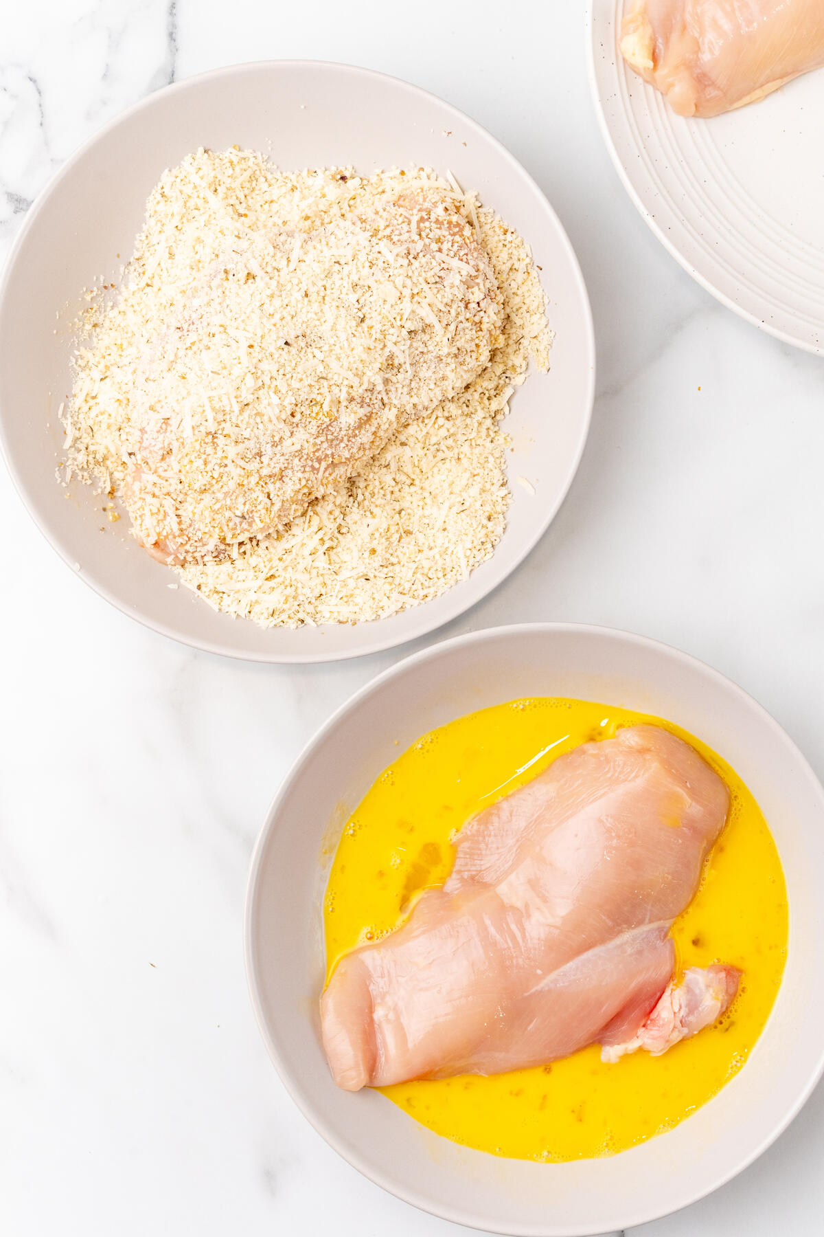 Preparation of Chicken Parmesan: raw chicken breasts in egg wash and a bowl of breadcrumbs.