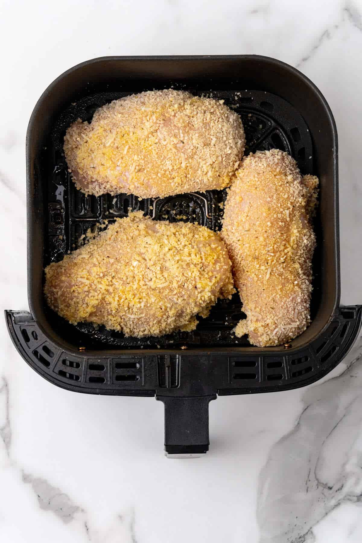 Three breaded Chicken Parmesan breasts in an air fryer basket.