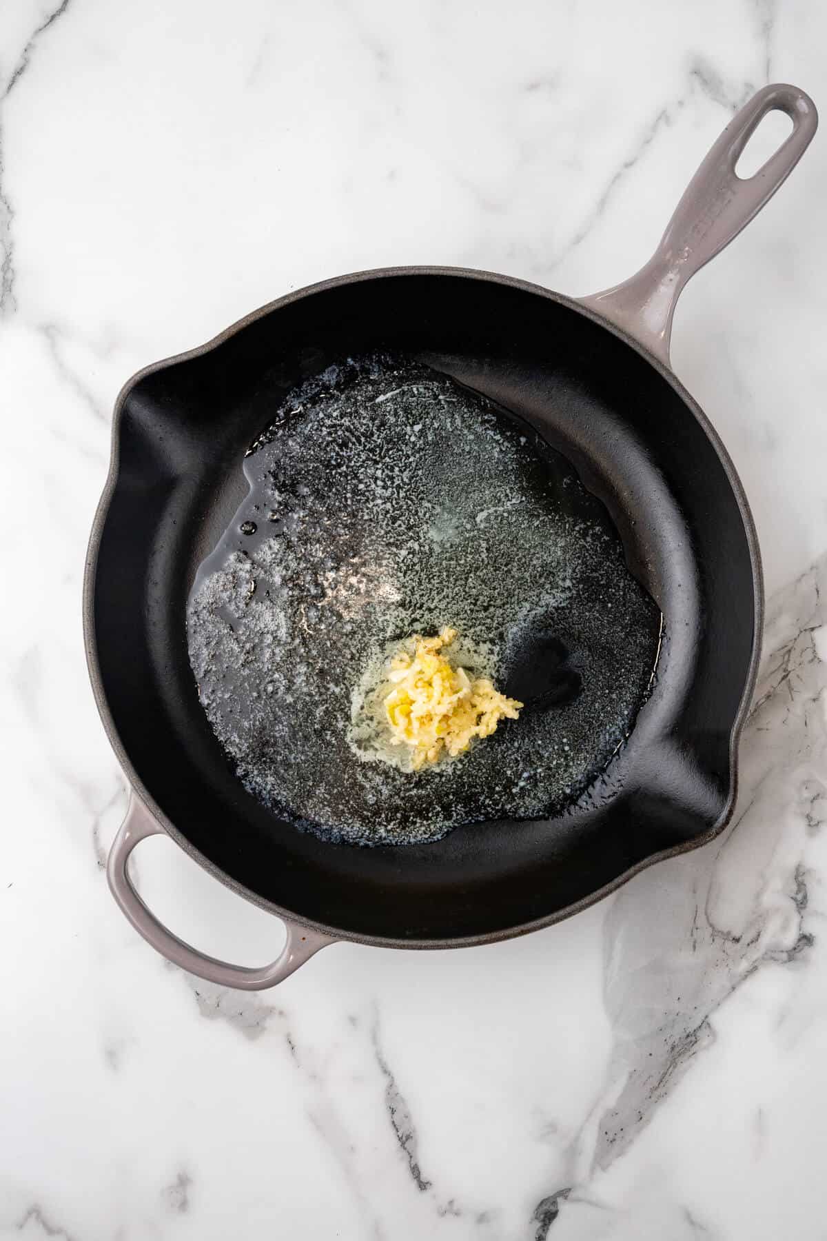 A skillet on a marble surface with melted butter.