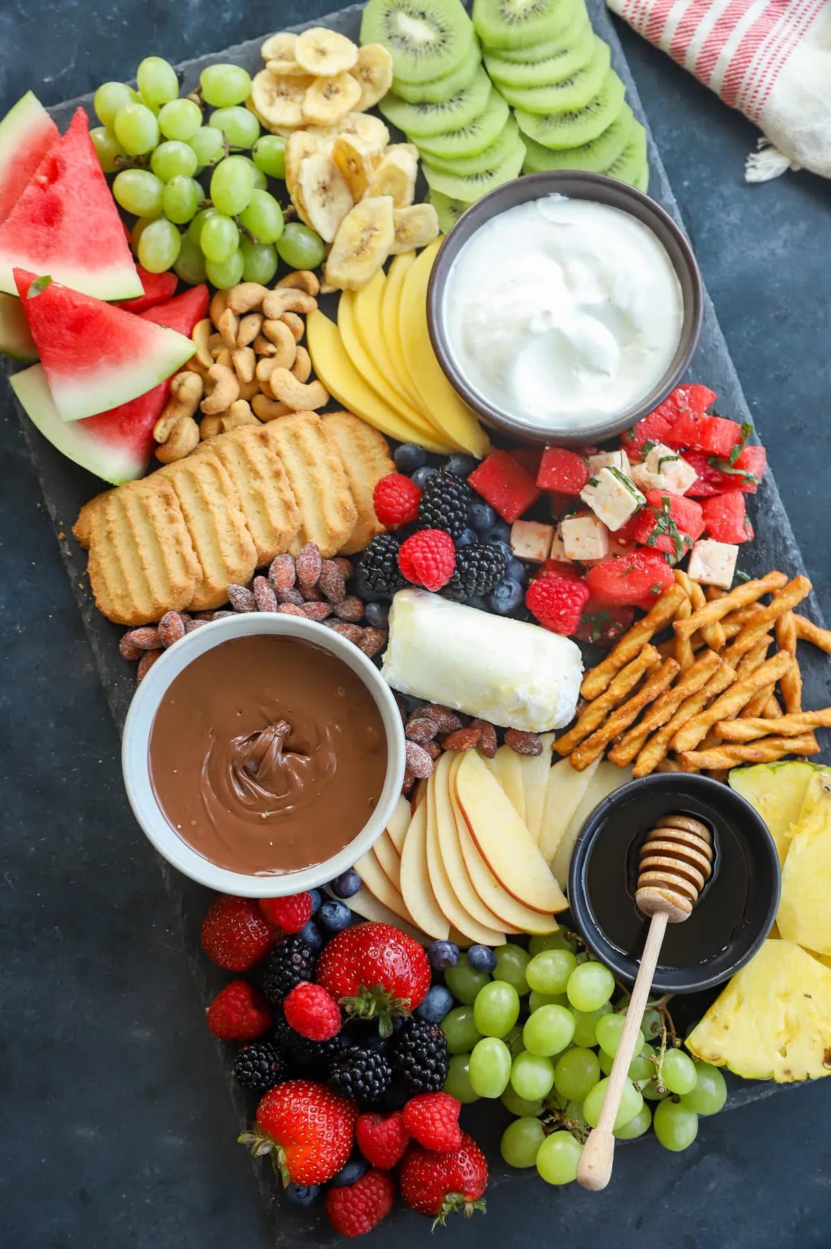 A colorful array of fresh fruits, nuts, and dips arranged on a dark surface for snacking.