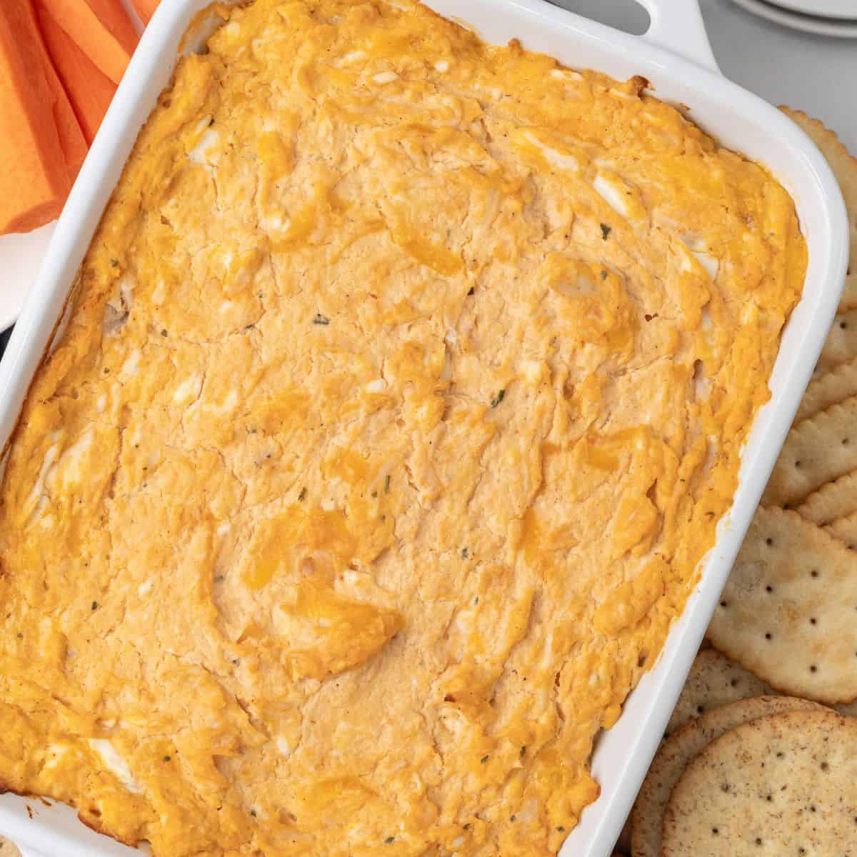 Creamy cheesy hot wing dip in a white dish with crackers, perfect for a snack or appetizer.