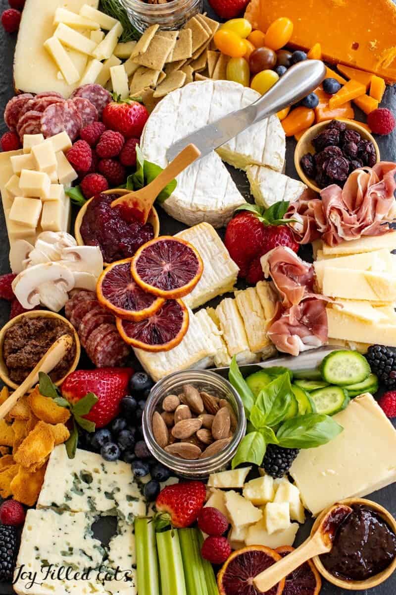An assortment of cheeses, cured meats, fruits, and nuts arranged on a wooden board for a charcuterie spread.
