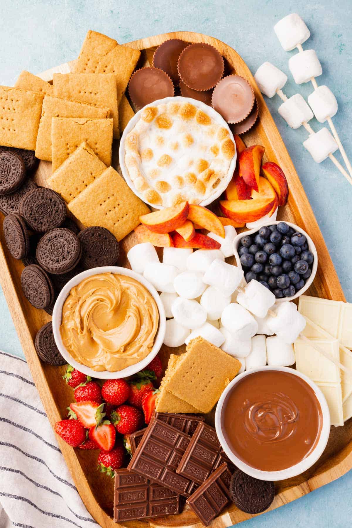 A variety of sweets and snacks including fruits, chocolates, marshmallows, and cookies arranged on a wooden platter for a dessert spread.