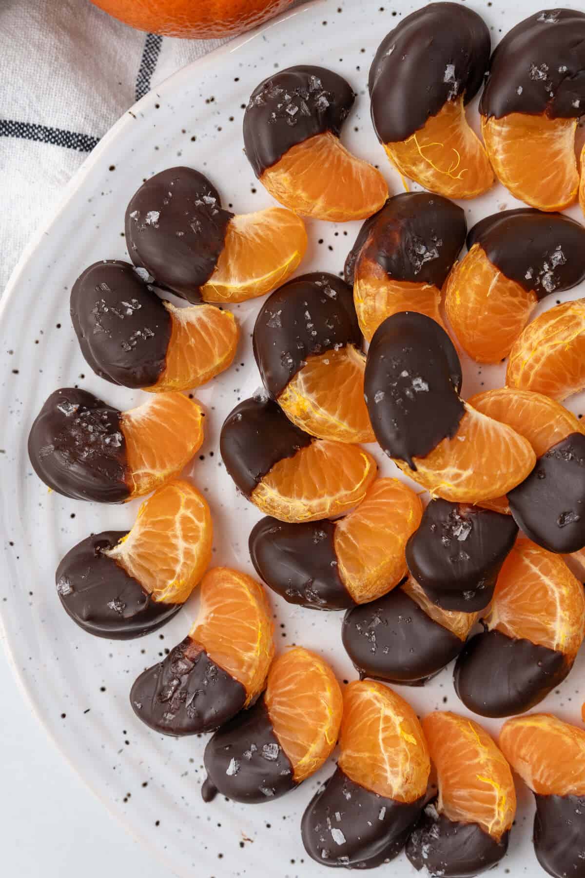 A top-down view of chocolate covered oranges on a white plate. 