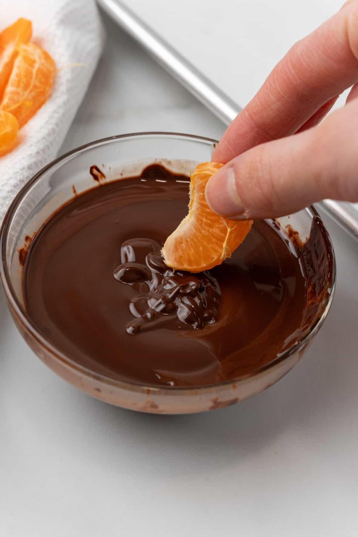 Orange being dipped into melted chocolate. 