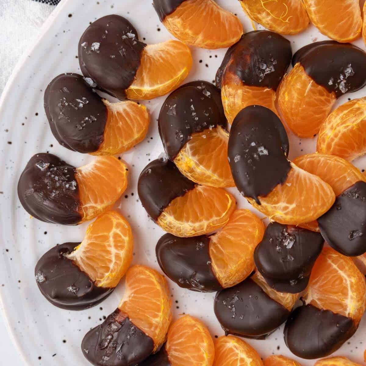 Chocolate covered orange slices dipped in dark chocolate and sprinkled with sea salt, arranged on a white plate.