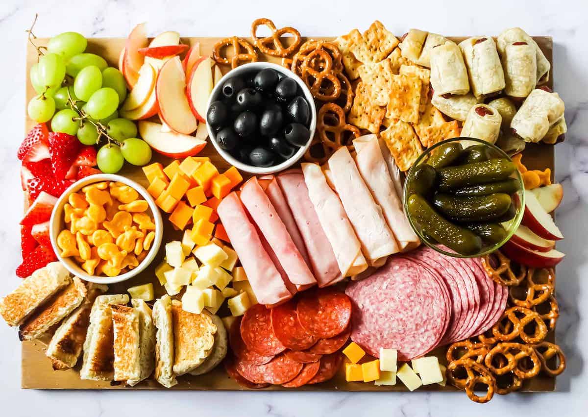 An assorted charcuterie board with a variety of meats, cheeses, fruits, and crackers.